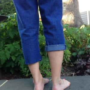 Back view of denim capris with one cuffed and one pegged leg. 